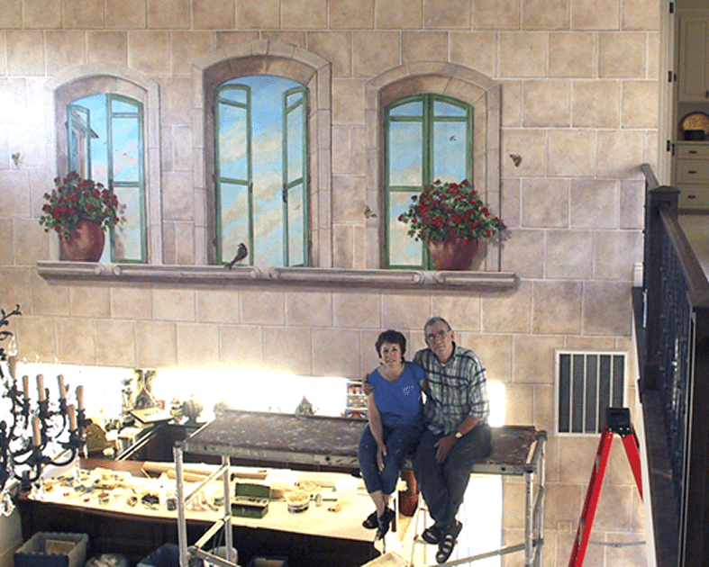 Two people pose near painted wall scene